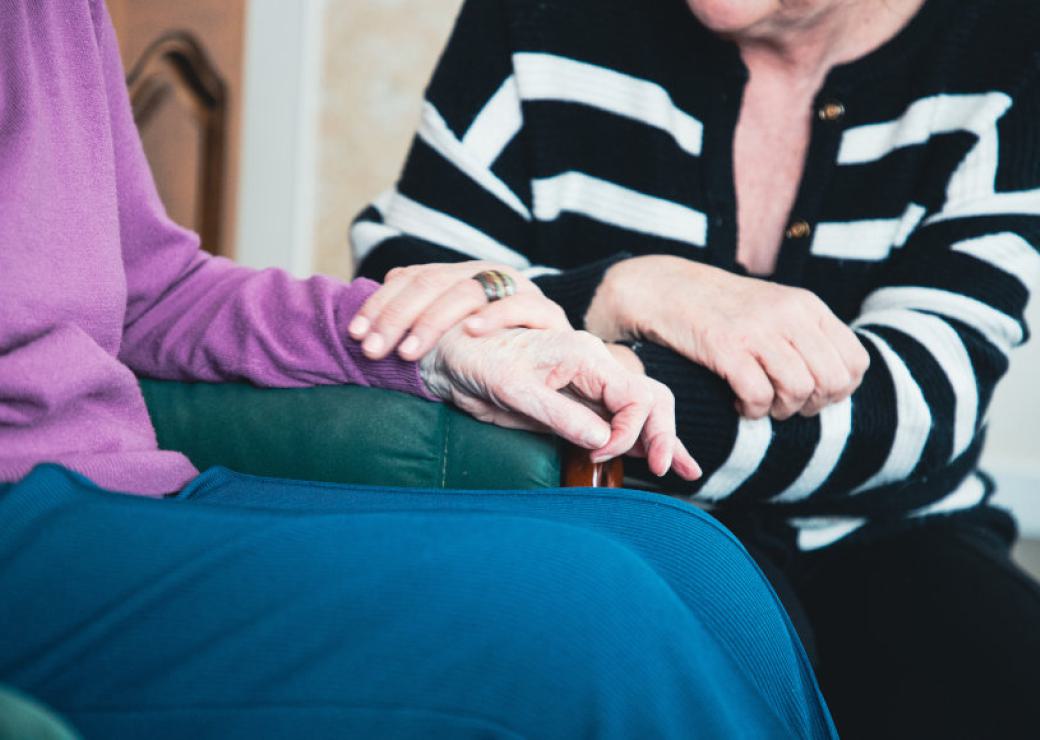 plan rapporché, pas de visages visibles, deux personnes se tiennent les mains. Une des personnes a beaucoup de rides sur les mains