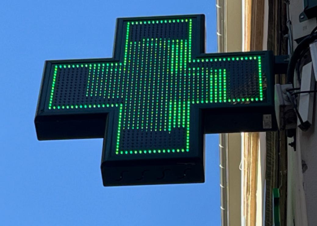 Une enseigne lumineuse enforme de croix verte, sur fond de ciel bleu