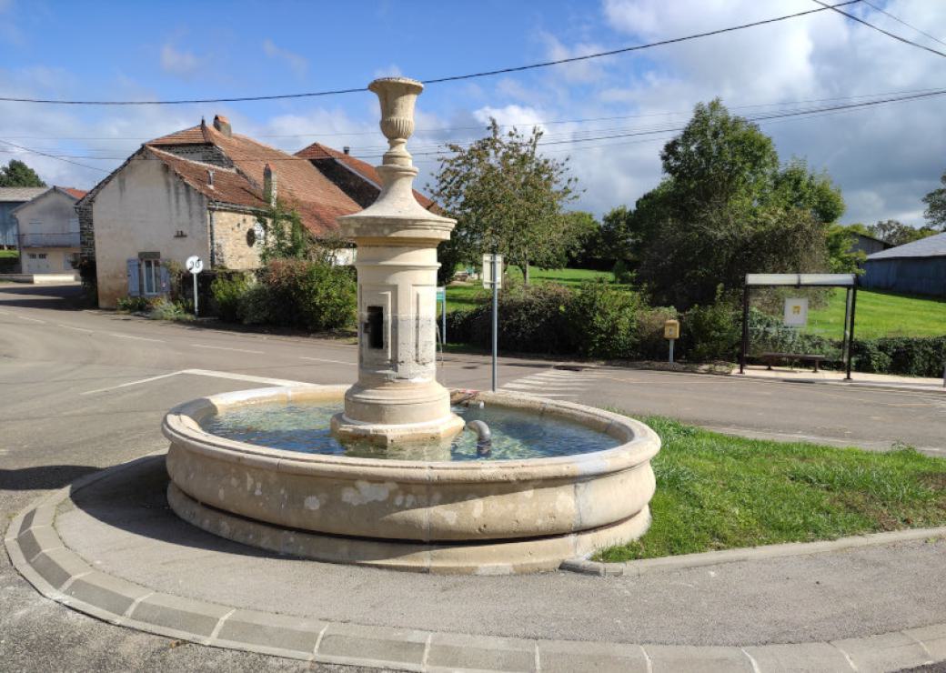 Une fontaine avec un bassin rond, sur un terre-plein entre des rues