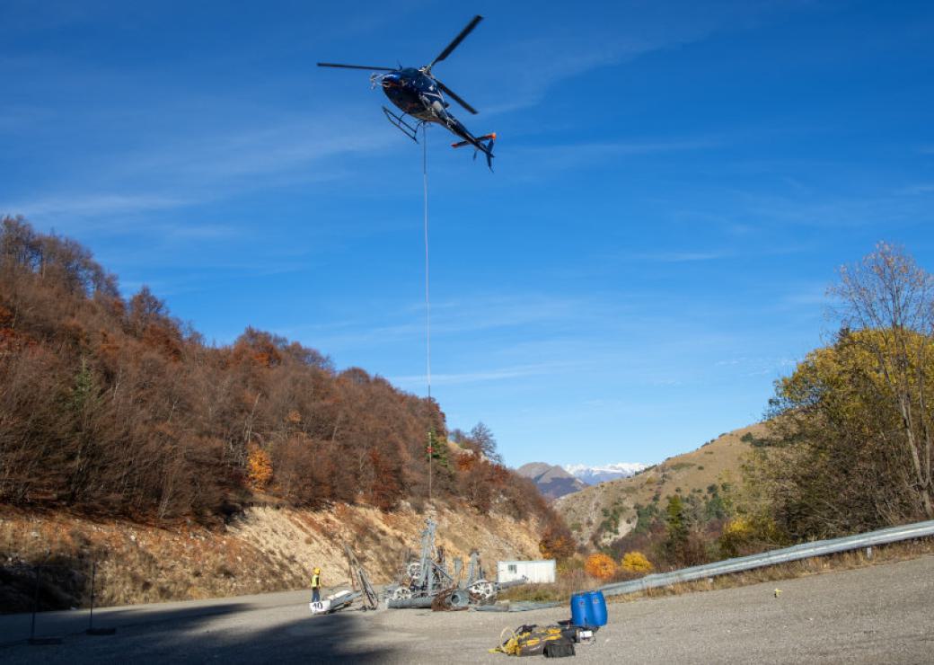 Un hélicoptère tracte un pylone, dans une zone entourée de montagnes