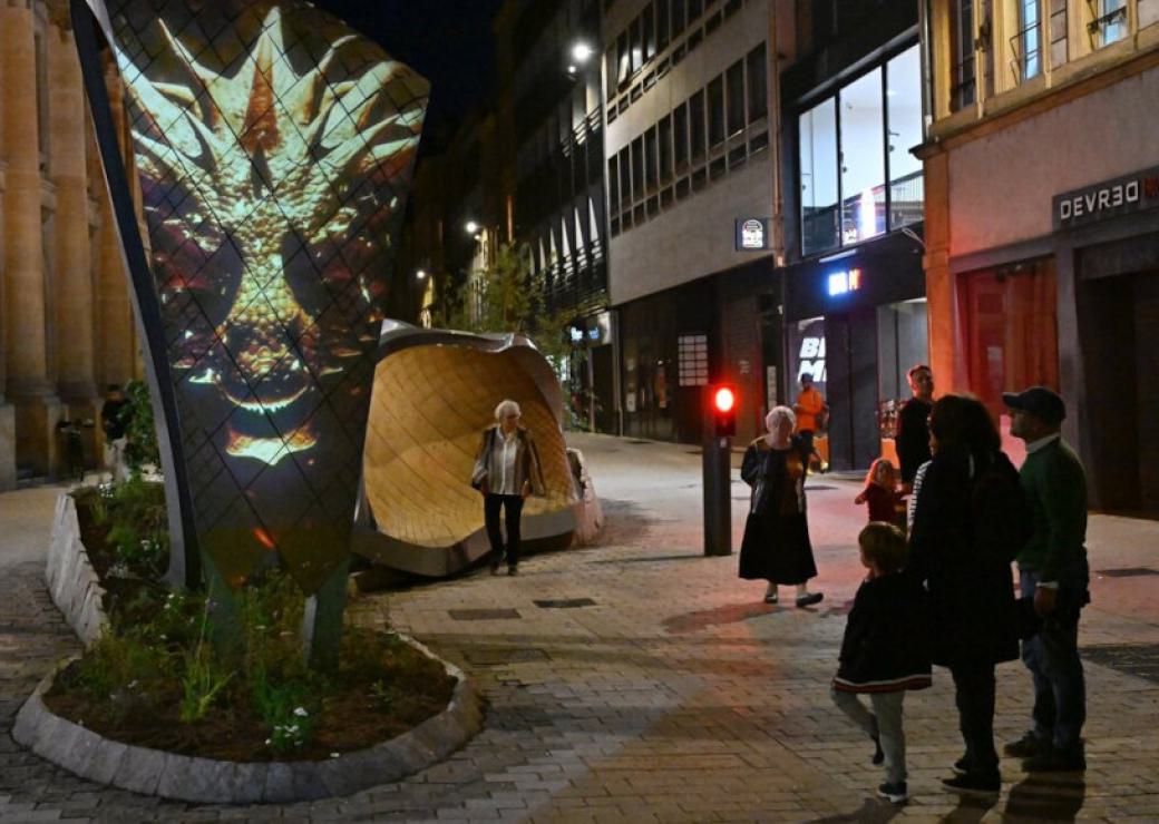 Des personnes dans une rue piétonne. En fond, un banc au design très moderne