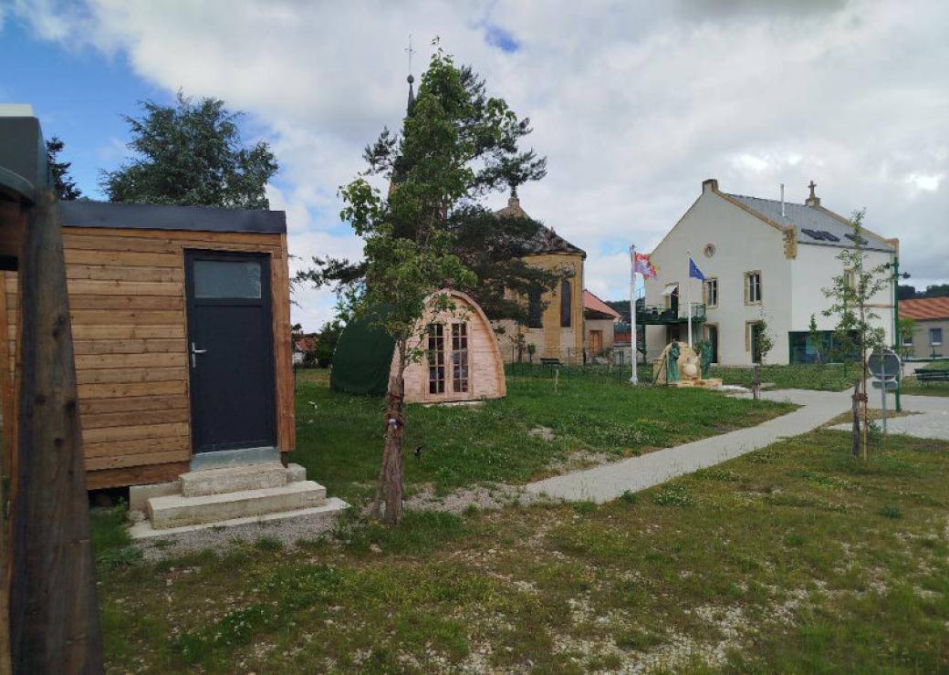Des petits habitats de bois sur un espace engazonné, et en fond une bâtisse d'habitation