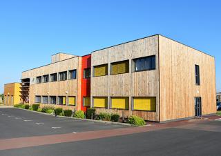 Un bâtiment, parallélépipède rectangle de 2 étages, bardé de bois doré, sur fond de ciel bleu.