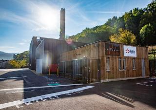 Photo d'un bâtiment industriel dont la façade est bardée de bois. Une grande cheminée s'en élance.