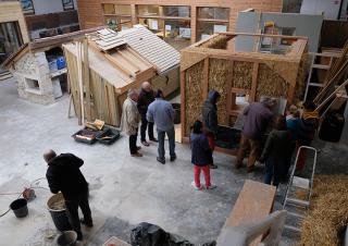 Vue de haut d'un très grand atelier où des personnes regardent des modèles de construction en bois et en paille