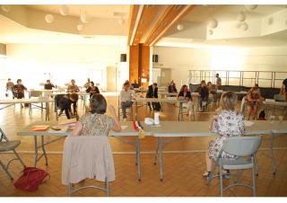 Dans une très grande salle, des personnes sont assises à des tables disposées en un grand cercle