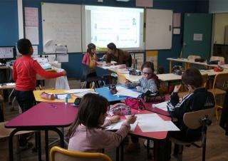 La photo montre une classe où les tables sont installées en étoile, avec des enfants en mouvement