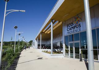 Une rangée de réverbères à gauche délimitent le chemin qui borde une façade moderne sur laquelle on peut lire "Eco campus Provence"