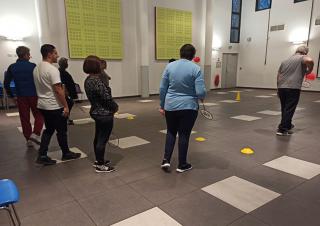 Huit personnes de dos dans une grande salle tiennent à la main une raquette de badminton