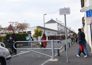 Vue d'une rue fermée par une barrière métallique, où des adultes marchent à côté d'enfants