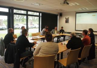 Dans une salle de réunion, une dizaine de personnes sont assises autour d'une grande table