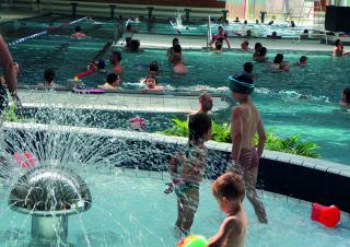 Vue intérieure d'une piscine. On dénombre une vingtaine de personnes dans les bassins.