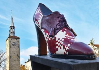 Plan large d'un soulier géant au premier plan, avec en fond une tour carrée surmontée d'un clocher