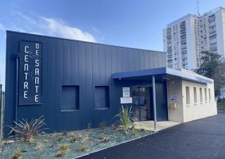 Photo d'un bâtiment moderne sur lequel on peut lire "Centre de santé". En arrière plan, une tour d'habitation