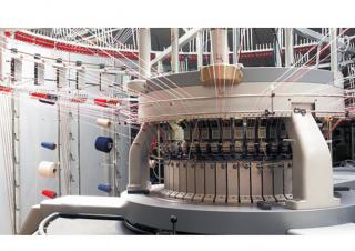 Photo d'une machine dont le centre est relié à des gros cônes de fil de différentes couleurs