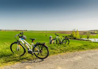 Sur un chemin de campagne, deux vélo blancs sont posés sur la béquille. Ciel bleu et herbe verte.