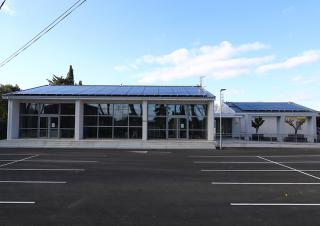 Photo d'un bâtiment moderne dont le toit est équipé de panneaux solaires. Devant le bâtiment, un grand parking goudronné