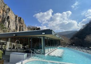 Plan large sur une piscine en plein air, où l'on voit l'eau bouiller. Le batiment moderne attenant est adossé à une falaise