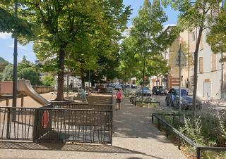 Photo d'une aire de jeux pour enfants, ombrée de platanes et bordée de bâtiments anciens