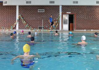 Dans une piscine, un homme montre des mouvements à des personnes immergées et coiffées d'un bonnet de bain