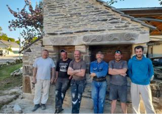 Six hommes en tenue de chantier se tiennent devant un four construit en pierre. 