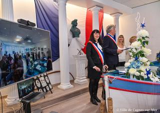 Une cérémonie civile de mariage. Deux élus ceints de leur écharpe et à leur côté un très grand écran montre la scène