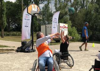 Sur un terrain en extérieur, deux personnes en fauteuil roulant jouent au basket