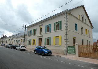 depuis la rue, photo d'une bâtisse de deux étages aux volets peints en vert, jaune et bleu