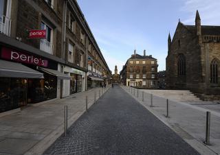 Une rue pavée de centre-ville, bordée de bâtiments de deux étages, avec des commerces en rez-de-chaussée. 