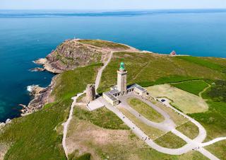 Vue aérienne d'un cap sur lequel sont dessinées des routes de sable au milieu d'un tapis vert. Au centre, se trouve un phare. L'ensemble est très géométrique