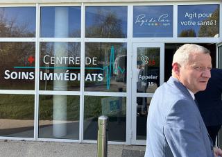 Un homme se tient devant une vitrine sur laquelle on peut lire : centre de soins immédiats Pays de Gex agit pour votre santé