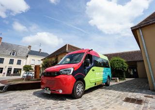 Sur une place de village, un utilitaire type minibus peint en rouge noir vert et bleu