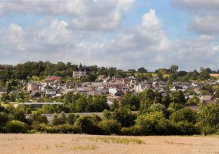 Au premier plan un champ de céréales blond, puis un village entouré d'arbres aux feuilles vertes