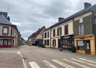 Rue d'un village, bordée de maisons à un étage, commerces en rez-de-chaussée