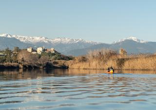 AU premier plan une étendue d'eau, puis un village perché sur une colline et au fond, des montagnes enneigées