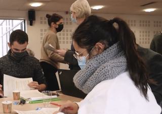 Des personnes portant un masque chirurgical sont assises à des tables et analysent des documents