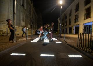 Un groupe de personnes emprunte un passage piéton. Il fait nuit et les bandes blanches émettent de la lumière