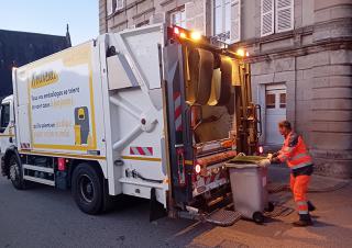 Une homme habillé en vêtements orange pousse une poubelle vers un camion benne