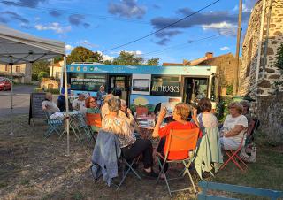 Une dizaine de personnes sont attablées à une terrasse installée devant un bus 