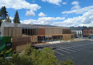 Un grand bâtiment moderne bardé de bois et longé par un parking