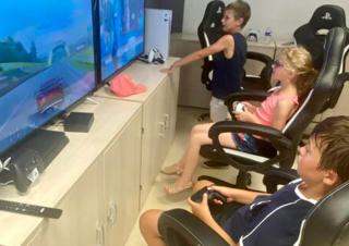 Trois enfants devant de grands écrans de jeux vidéos