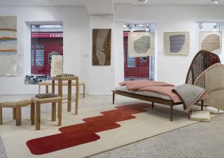 Showroom avec au sol un tapis, des couvertures pliées sur une banquette et des tentures aux murs