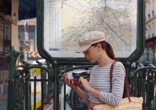 Une touriste en train de regarder son smartphone devant une entrée de métro 