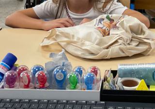 Sur le bureau d'un écolier, un sac de toile et des pots de gouache de couleur