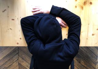 Vue de haut d'une personne, capuche sur la tête et tête reposant sur la table, avec les bras autour