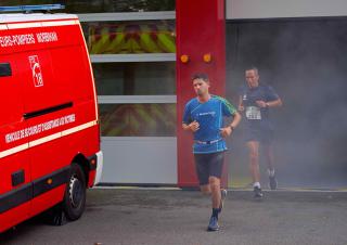 Une homme sort en courant d'un bâtiment enfumé, devant lequel est garé un camion de pompiers