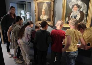 Un groupe d'enfants devant deux tableaux - portraits de femme