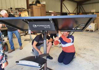 Dans un hangar, des personnes sont agenouillés et intervienne sur le pied d'un panneau solaire