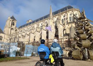 Des personnes installées sur un vélo deux place regardent une cathédrale