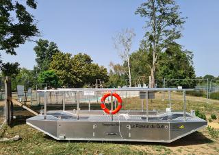 Une barge métallique à fond plat est posée sur la berge d'un cours d'eau